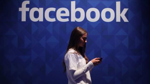 A woman using her phone under a Facebook logo (file image)