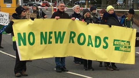 Extinction Rebellion protestors holding up 'No New Roads' banner and blocking the vehicle entrance to Norfolk County Hall
