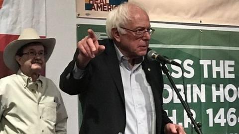 Bernie Sanders stands in front of a microphone, pointing as he speaks.