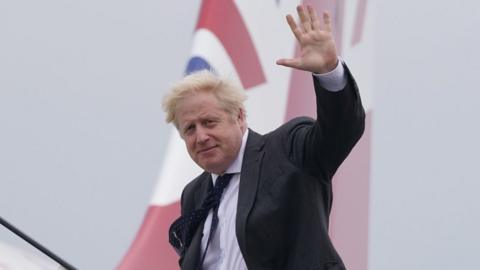 Boris Johnson waving as he boards a plane to New York