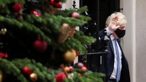 Boris Johnson waves outside Downing Street, with a Christmas tree in the foreground, 8 December 2021