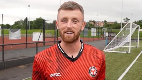 Omagh-Town player-manager Caolan McAleer talking to the camera at a football pitch