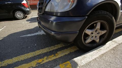 A dark coloured car is parked on double yellow lines. 