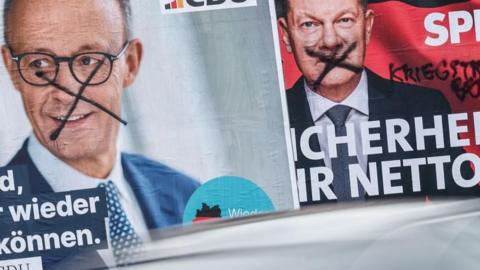 Two posters on a street in Berlin show the conservative Friedrich Merz (L) and rival Social Democrat Olaf Scholz - both have been defaced with black X marks on their faces