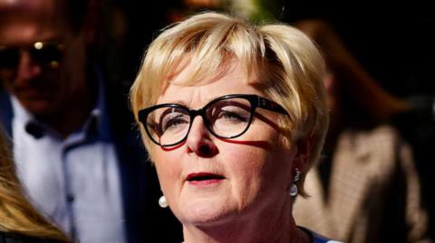 Linda Reynolds, wearing black-rimmed glasses with short blonde hair 