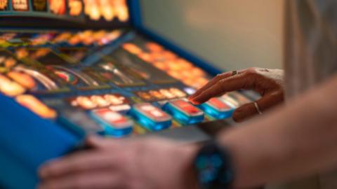 Hands pressing buttons on a fruit machine.