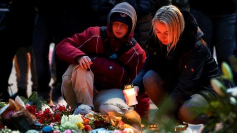 A woman holds a candle as people leave floral tributes to the victims near the site where a car rammed into a crowd at a Magdeburg Christmas market in Magdeburg, Germany