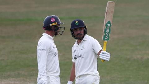 Glamorgan batter Kiran Carlson raises his bat stood next to Colin Ingram having scored 50 against Leicestershire