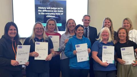 Nine women and one man are smiling, with six women holding up certificates.
