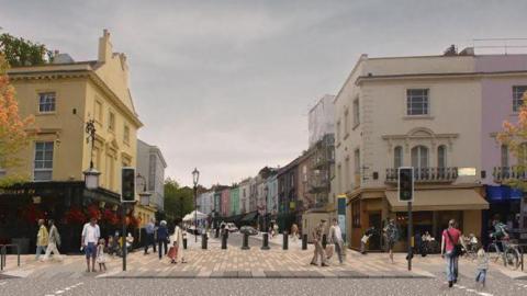 An animated mockup image of Portobello Road. There is a row of multicoloured two-storey buildings on either side of the road, some with shops and awnings below. In front of the road is a pedestrianised walkway with two traffic lights on either side. There are people on the walkway and on adjacent pavements.