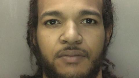 Mugshot of Rhemeese Lawrence-Hayden against a beige backdrop. he has a expressionless face and looking straight into the camera