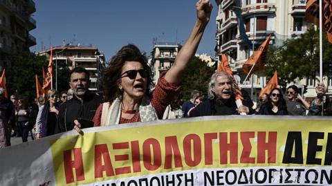 A group of people holding a banner as they march during a protest in Greece.