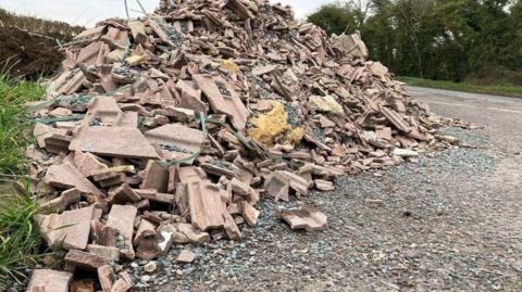 a pile of bricks and tiles in a lay-by by the side of a road next to a grass verge