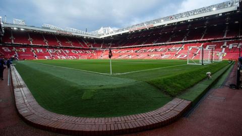 An image of an empty Old Trafford taken from near the corner flag and looking towards the Stretford End and the Sir Alex Ferguson Stand. The bricks that are below the run-off area are in the foreground.