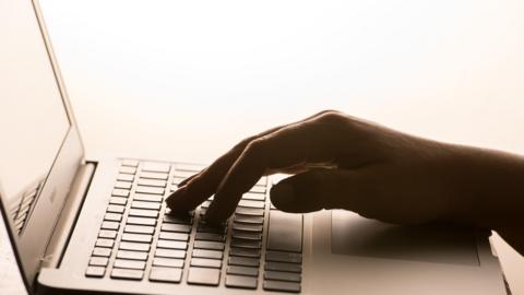 A picture of a hand typing on a keyboard. It is a silver laptop.