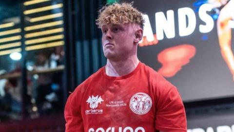 Jake Orr, a man with blonde curly hair, is pictured in a red sports top.