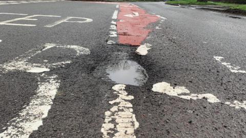 A large and deep pothole filled with water in the middle of a road.
