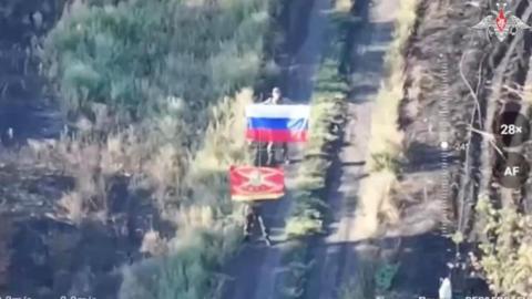 A fuzzy image of two men holding Russian flags on a road - one of the flags is a tricolour the other is a red military flag