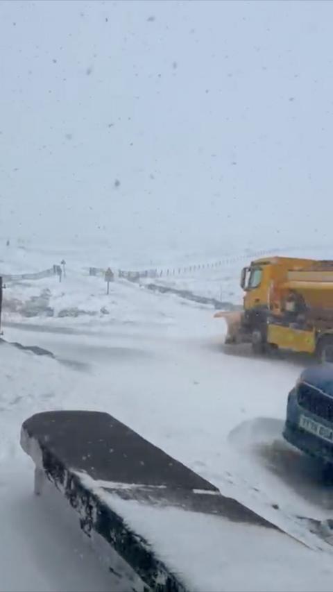 Snow covered hills and a yellow snowplough in the background.