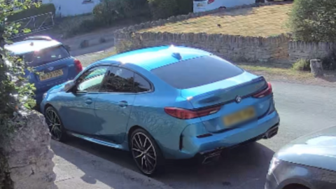 Paul Mason's metallic blue BMW M2 parked outside his house before the theft. The car is a five door vehicle and is parked between two other cars.