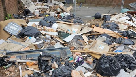 Black bin bags, rubble and cardboard strewn across car park
