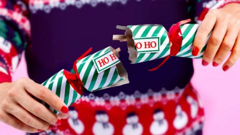 Close up of a person with red nails pulling a cracker with the words 'ho ho ho' on it