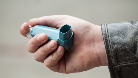 A hand holding a blue inhaler with the sleeve of a leather jacket visible