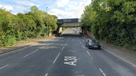 A view of Barnwood Road from Google maps with a car on the road, and a railway bridge with a freight train crossing it.