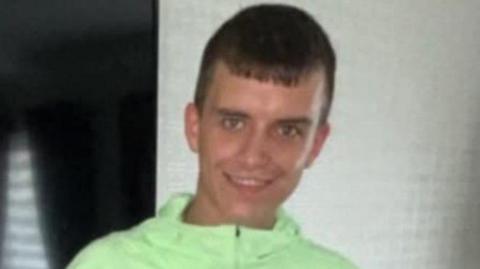Robert McNally smiles at the camera - he has dark, cropped hair and a light green jacket or tracksuit top on