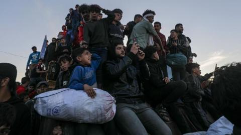 A group of men and children sit atop a vehicle with their belongings