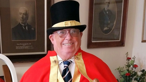 Terrence Mullett in town crier regalia - wearing red robes and black top hat and glasses