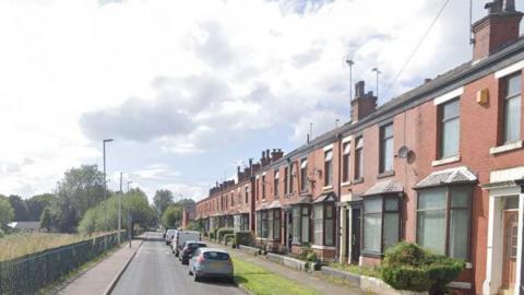 A street with parked cars and terraced housing on the right hand side of the road 