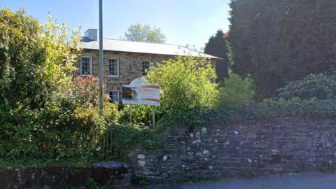 A sign reading St Petroc's Care Home is in front of a stone built two storey building.