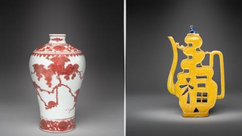 A red vase with a white base, with grapevines and squirrels. It is next to a yellow wine pitcher moulded in the combined Chinese characters meaning good fortune and longevity. 