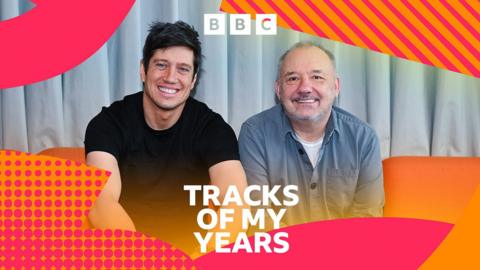 Vernon Kay and Bob Mortimer sit side by side on a sofa and smile at the camera.