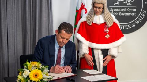 Rhun signing with a High Court judge watching over him