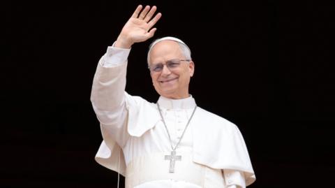 Pope Leo waves wearing all white on a black background