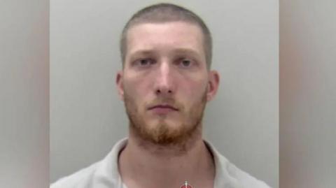 Young man with short cropped hair and a ginger beard looking to camera.