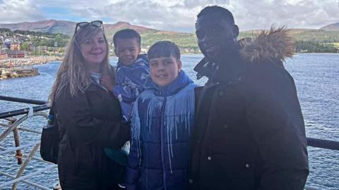 Harriet with Leon, JJ and Sulaimon standing in front of a lake with hills in the background