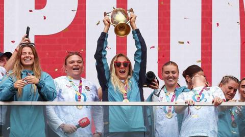 Zoe Aldcroft lifts the Women's World Cup trophy as she celebrates with team-mates at Battersea Power Station 