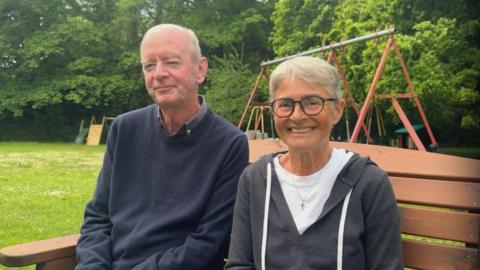 Peter and Helena McGovern, sat on a bench in what looks like a garden or a park.