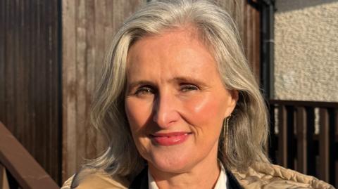 Eilin Casey. A head and shoulders shot of a woman with shoulder-length silver hair and pink lipstick