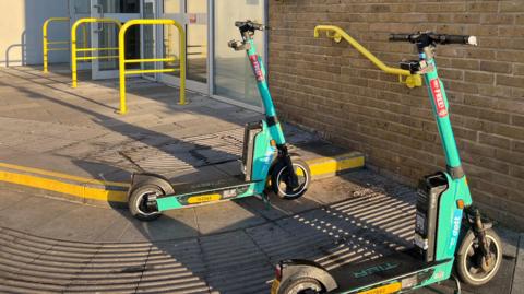 Two green Dott e-scooters parked outside Chelmsford railway station.