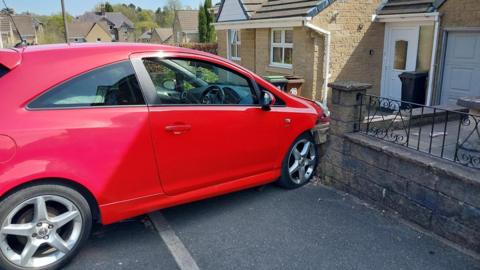A red car that has crashed through the stone fence outside a home