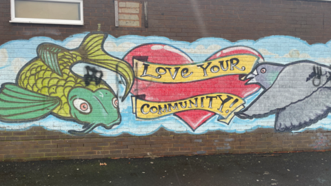 A spray painted green fish, grey pigeon and red love heart with the words "love your community" on a yellow spray painted ribbon.