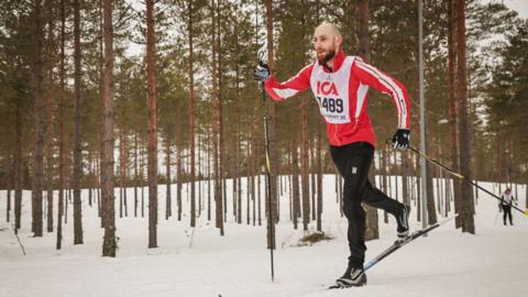 Matt Ireland in red and white gear is skiing through a snowy forest.