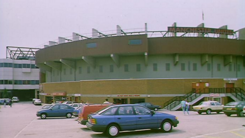 Cars parked by the side of Old Trafford underneath a red and black Manchester United sign in 1989