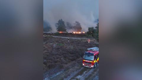Fire engine at heathland wildfire with firefighters battling flames