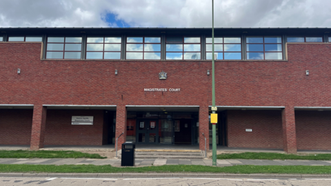 Newton Aycliffe Magistrates' Court. The building is made of red brick and has a sign showing its name and a black bin out front.