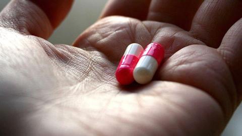 two red and white capsules sit next to each other in the palm of an open hand